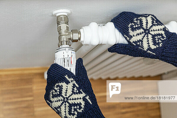 Hands of senior man wearing woolen gloves adjusting temperature of radiator
