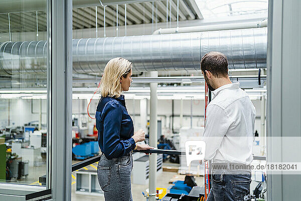 Business colleagues discussing with each other standing by railing in factory