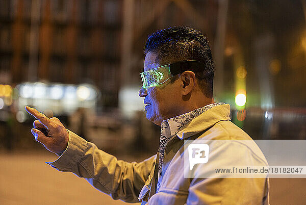 Mature man wearing smart glasses gesturing on footpath at night
