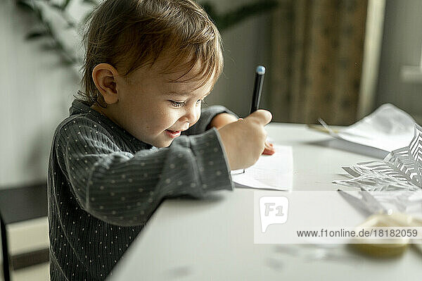 Junge zeichnet mit Bleistift am Tisch zu Hause auf Papier
