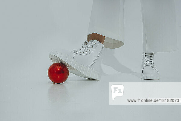 Teenage girl stepping on red Christmas ornament against white background