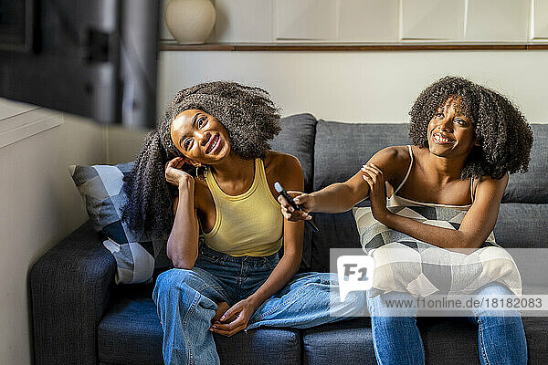 Smiling lesbian couple watching TV sitting on sofa in living room