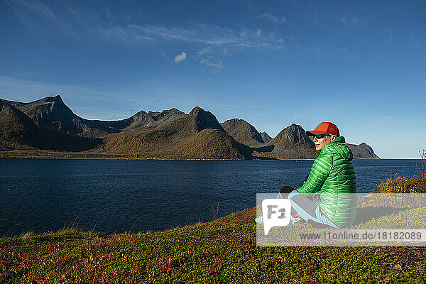 Thoughtful mature woman sitting by fjord on sunny day