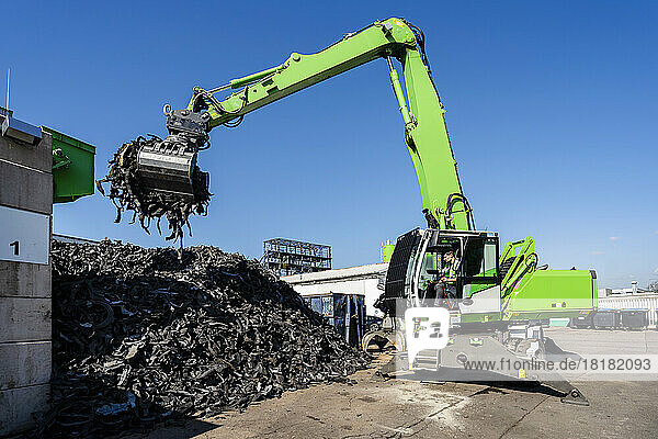 Mature man operating excavator and lifting rubber waste at recycling center