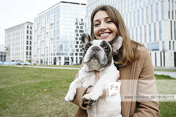 Happy woman carrying french bulldog in front of buildings