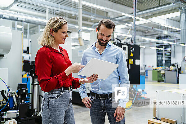 Smiling businesswoman explaining colleague over tablet PC at factory