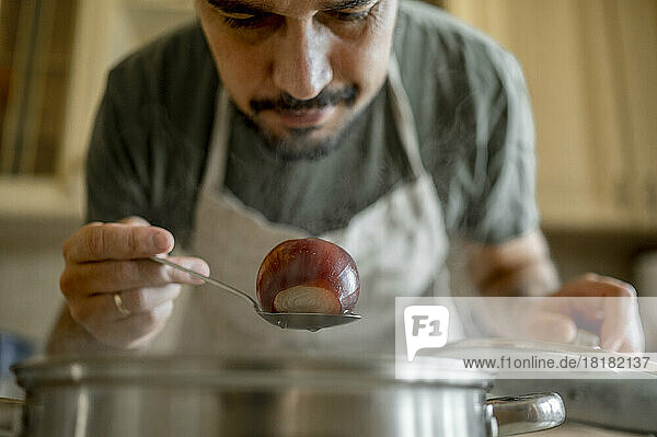 Man examining onion on spoon at home