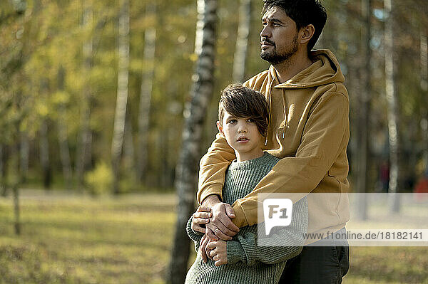 Father embracing son from behind in park