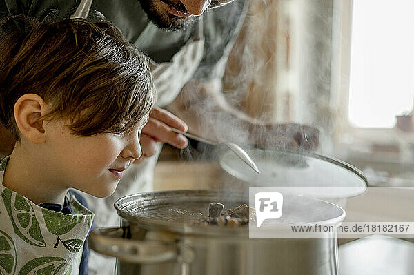 Boy looking at soup prepared by father in kitchen