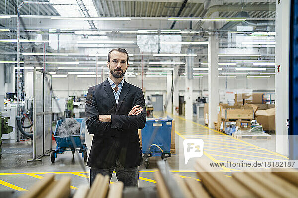 Confident businessman with arms crossed standing in factory