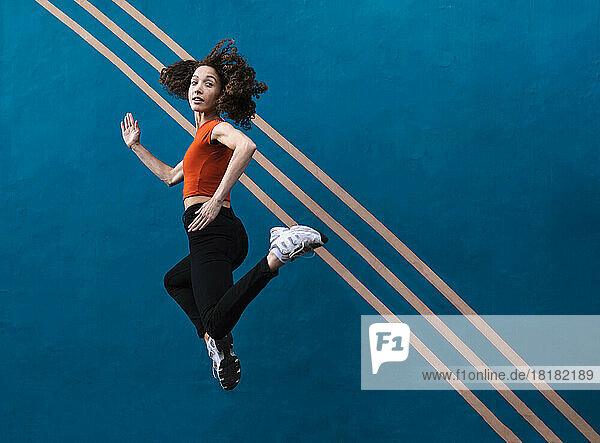 Woman jumping in front of blue wall