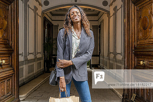 Smiling woman with shopping bags standing at doorway