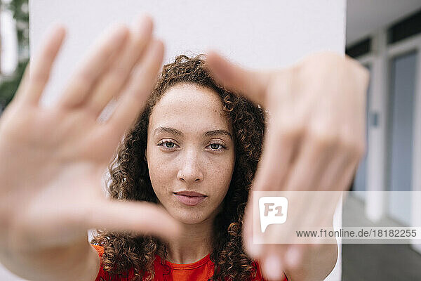 Smiling curly haired women looking through finger frame