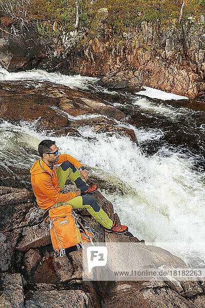 Mann mit Rucksack genießt es  auf einem Felsen zu sitzen