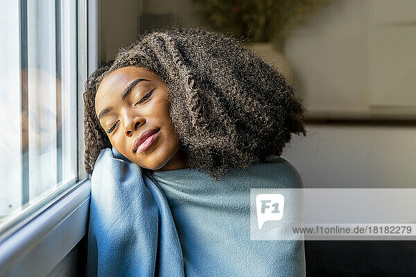 Frau  in eine Decke gehüllt  entspannt sich zu Hause am Fenster
