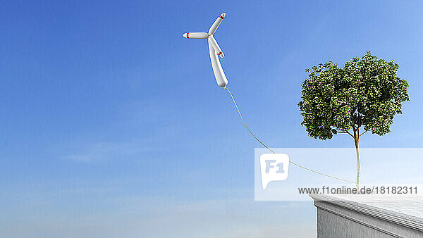 Wind turbine shaped balloon tied to single tree growing on rooftop