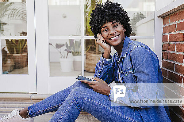 Happy young woman with smart phone sitting in doorway