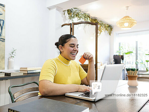 Happy woman with credit card doing online shopping through laptop on table