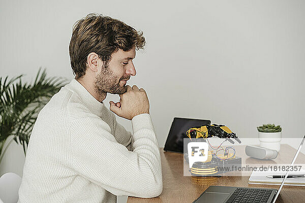 Engineer examining robotic arm on desk in office