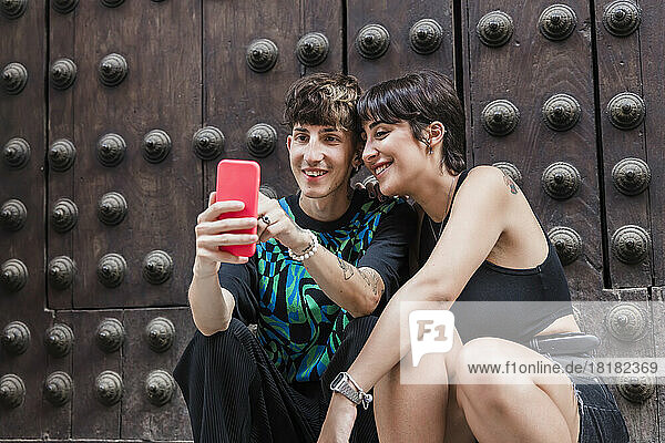 Happy man sharing mobile phone with girlfriend in front of door