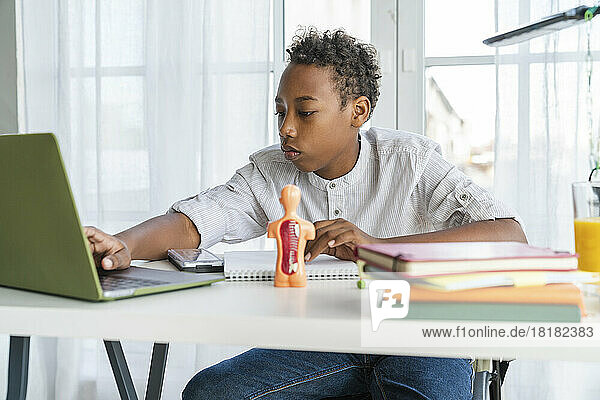Junge macht Hausaufgaben mit Laptop und sitzt zu Hause am Tisch