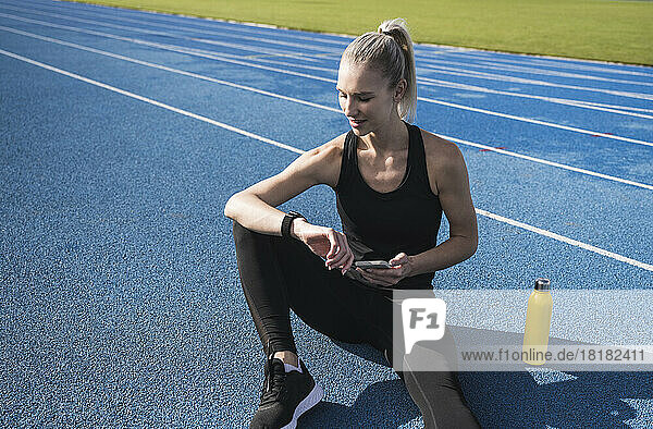 Sportswoman holding mobile phone checking time on smart watch on track