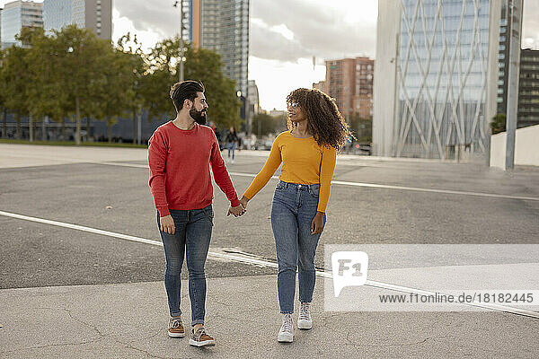 Junges Paar hält Händchen und geht am Fußweg entlang