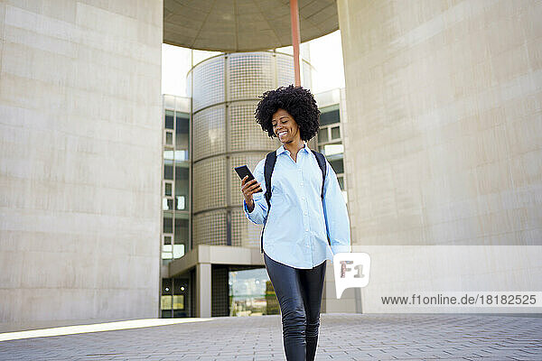 Happy young businesswoman using mobile phone outside building