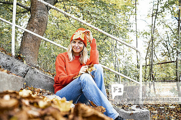 Mature woman with autumn leaf sitting by railing in park