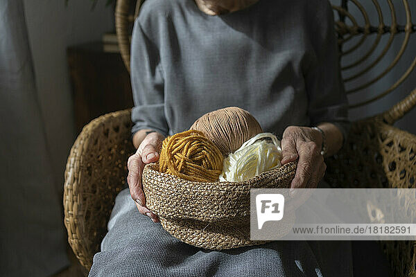 Hands of senior woman holding basket of colorful knitting wool at home