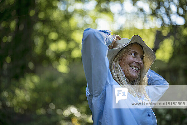 Cheerful mature woman adjusting hat in garden