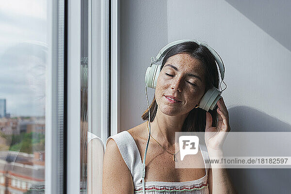 Junge Geschäftsfrau hört Musik über Kopfhörer am Fenster