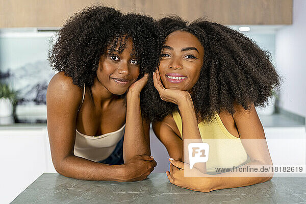 Multiracial lesbian couple smiling and leaning on kitchen island at home