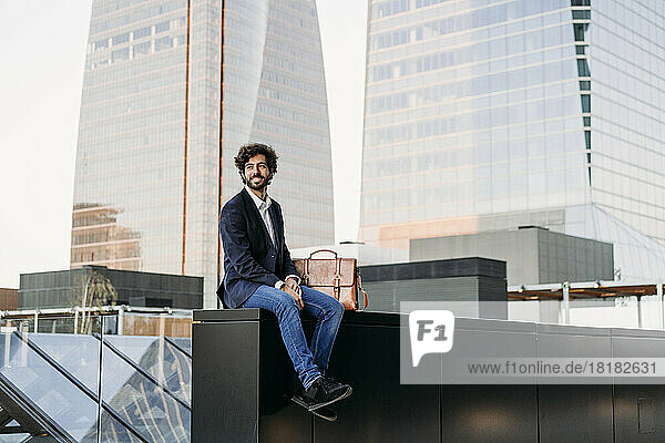 Businessman sitting on wall in front of building