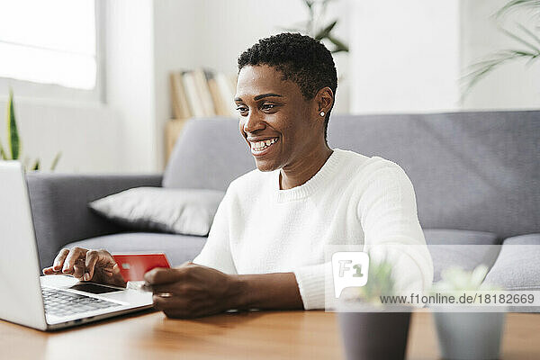Happy woman holding credit card and using laptop at home
