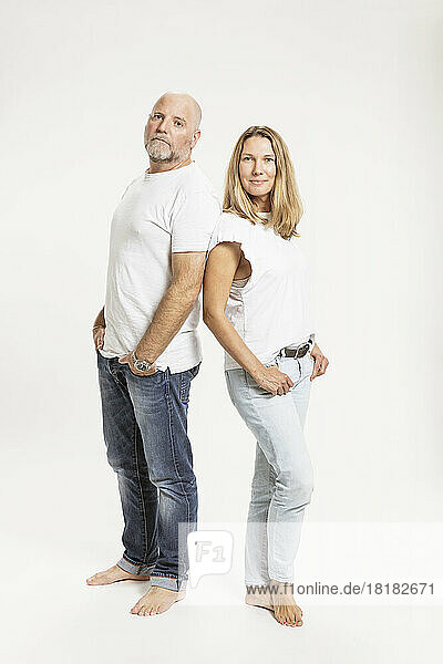 Confident mature couple with hands in pockets against white background