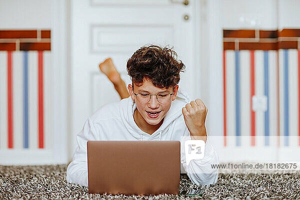 Happy boy gesturing fist looking at laptop