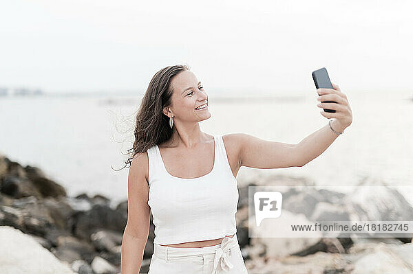 Lächelnde Frau macht im Strandurlaub ein Selfie per Smartphone