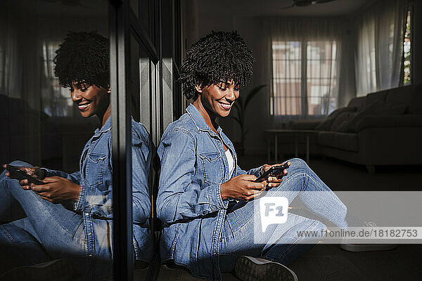 Happy young woman using smart phone sitting in living room at home