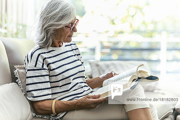 Woman reading book sitting on sofa at home