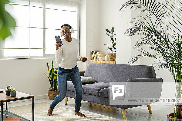 Carefree woman with mobile phone listening to music with headphones at home
