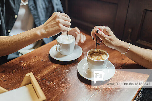 Hands of young couple stirring coffee in cafe