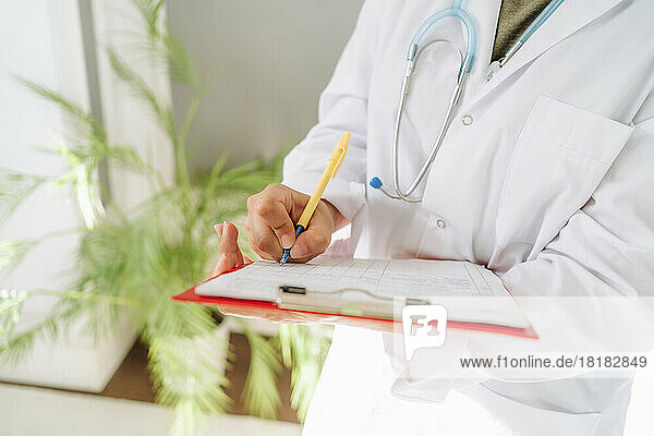 Doctor wearing lab coat writing prescription at clinic