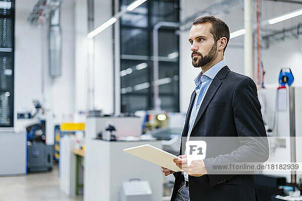 Young businessman with tablet PC standing in factory
