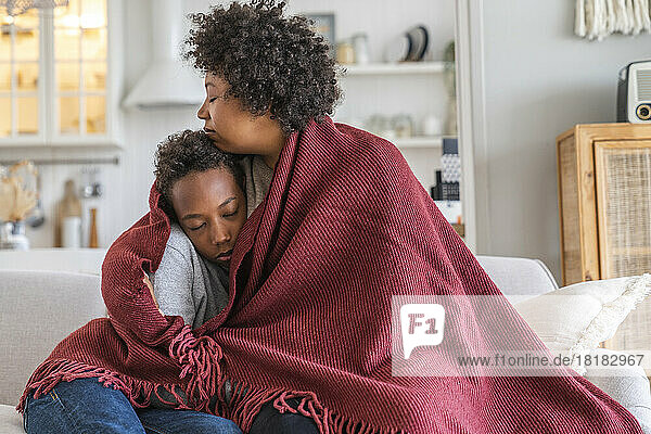 Mother sitting with son wrapped in blanket at home