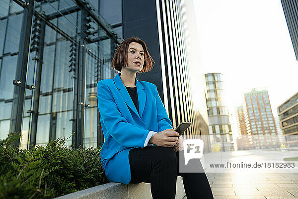 Businesswoman with smart phone sitting in front of office building