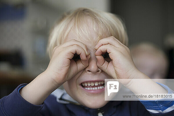 Portrait of smiling little boy looking through his hands formed like spectacles