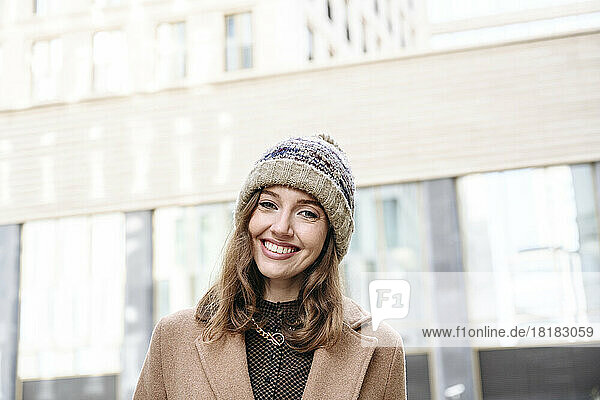 Happy woman wearing knit hat standing in front of building