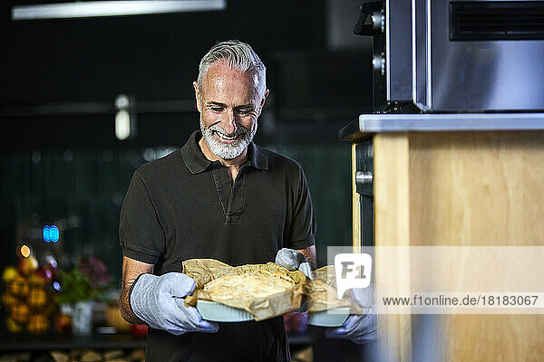 Happy man standing with savory pie by oven in kitchen