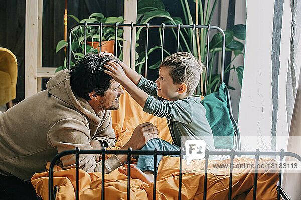 Son adjusting father's hair on bed at home